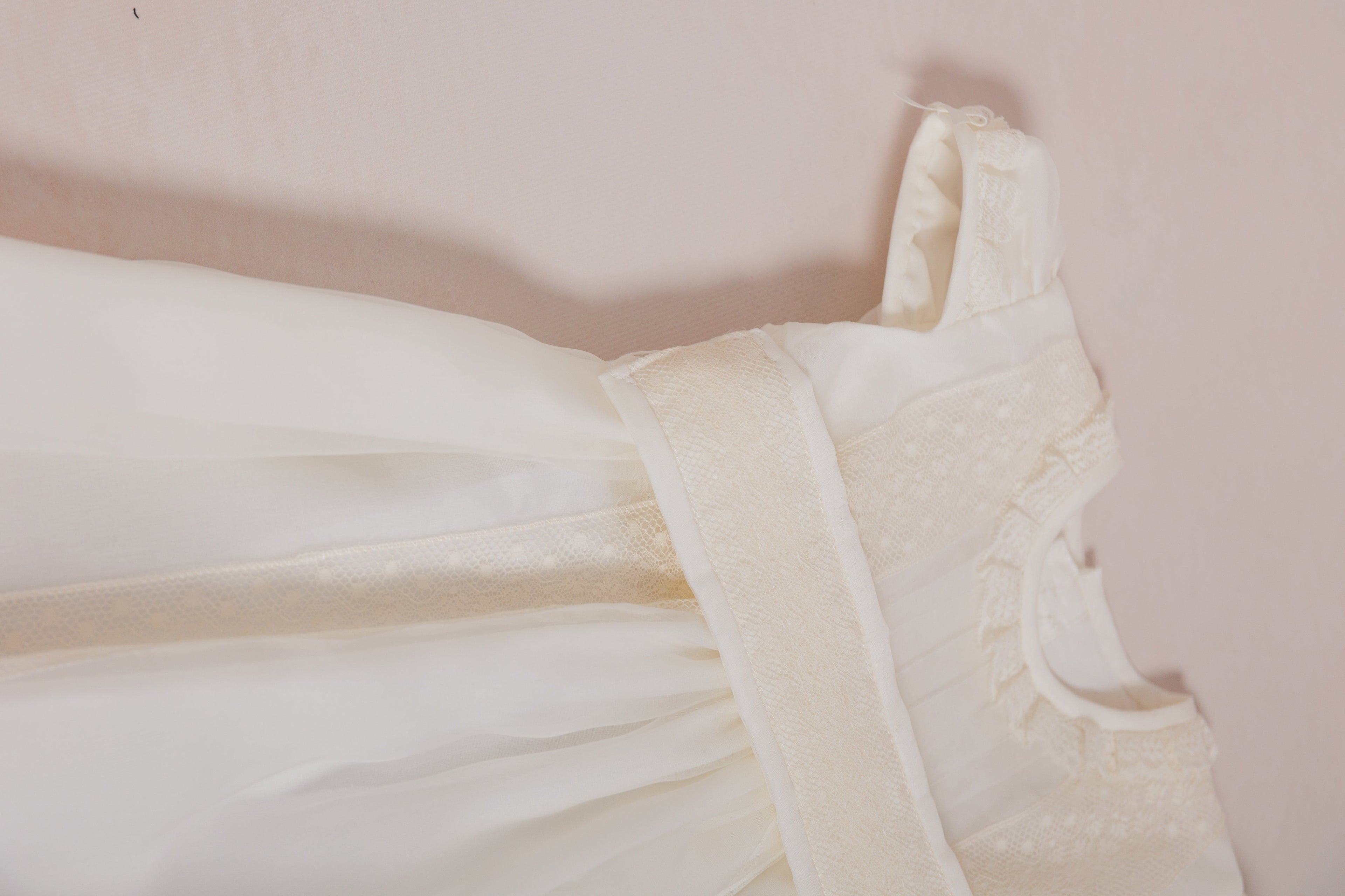 White babtism dress with lace details on a light pink background